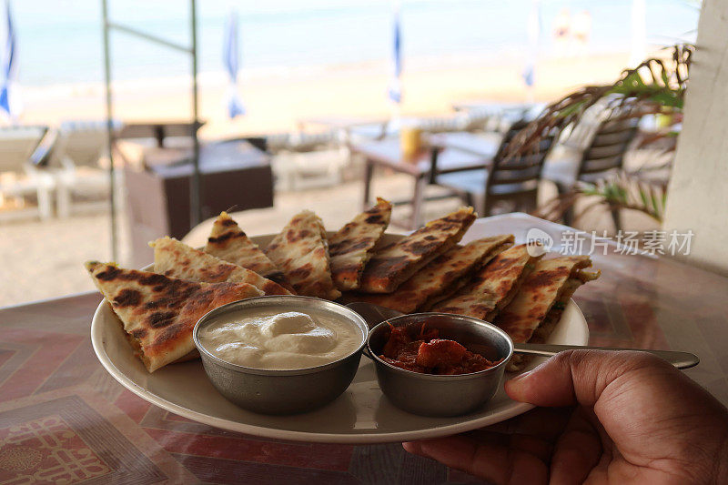 印度自助早餐的形象，三角形的aloo paratha切片和焦糖洋葱撒，白色盘子由一个不认识的人，美味的面包塞满了garam masala土豆，酒店餐厅aloo paratha菜，raita凝乳酸奶